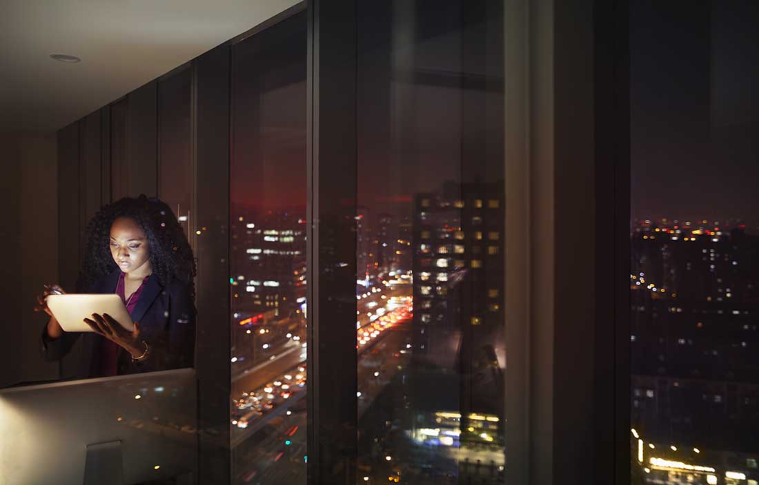 Business professional looking at tablet computer at nighttime.