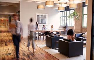 Image of a bustling modern office, with various seating options and staff doing in-person work.
