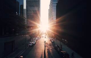 Aerial view of a city street bracketed by skyscrapers at sunset with the sun peaking between the buildings