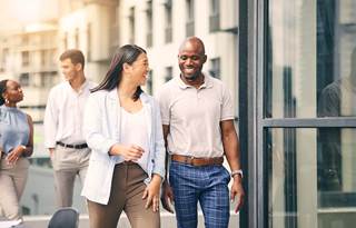 Two office workers walking outside an office building, laughing, with people in the background
